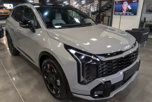 Kia Sportage 2025 gris céramique avec toit noir, vue 3/4 avant droit, calandre et phares modernes en showroom.