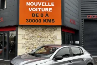 Peugeot 208 PureTech 100 S&S Active gris clair vue 3/4 avant droit devant un bâtiment avec panneau orange Distinxion.