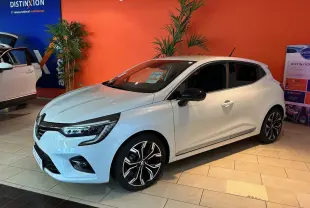 Renault Clio V blanc nacré métal vue 3/4 avant droit en showroom avec jantes alliage noires et chromées.