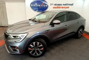 Vue 3/4 avant droit d’un Renault Arkana gris clair Evolution E-Tech full hybrid 145 en intérieur showroom.