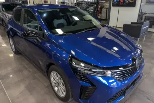 Renault Clio V Bleu Iron vue 3/4 avant droit en intérieur, avec calandre noire et phares LED distinctifs.