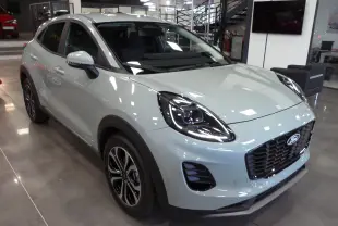 Ford Puma 2025 gris Cactus en 3/4 avant droit, avec phares LED et calandre noire brillante dans un showroom.