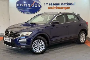 Volkswagen T-Roc bleu en 3/4 avant droit, avec jantes alliage et barres de toit noires visibles.