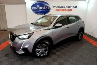 Peugeot 2008 gris clair vue 3/4 avant droit dans un showroom avec éclairage et logo Distinxion en arrière-plan