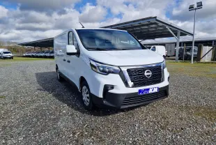 Vue 3/4 avant droit d’un utilitaire Nissan Primastar blanc avec calandre noire et logo Nissan visible, sur parking extérieur.