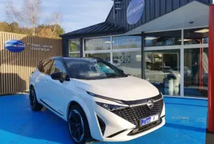 Nissan Qashqai Hybrid e-POWER 2025 blanc nacré toit noir, vue 3/4 avant sur sol bleu devant showroom Distinxion