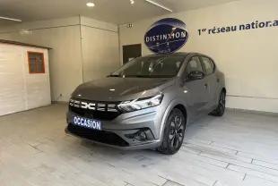 Vue 3/4 avant droit d'une Dacia Sandero gris métallisé 2025 avec calandre noire et jantes alliage noires.