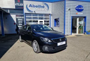 Peugeot 308 SW noire vue en 3/4 avant droit devant un garage avec enseigne Abeilhé autos.