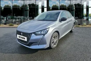 Peugeot 208 gris clair vue 3/4 avant droit, avec calandre noire et phares LED distinctifs.