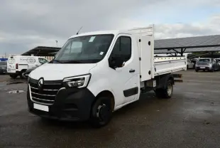 Renault Master blanc en vue 3/4 avant droit avec benne pick-up et pare-chocs noirs sur parking humide.