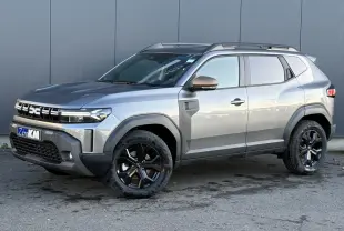 Dacia Duster 2026 gris schiste en vue 3/4 avant droit, avec jantes alliage noires et barres de toit longitudinales.