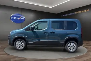 Vue de profil côté gauche du Peugeot Rifter bleu 2026 dans un showroom avec jantes argentées et portes coulissantes.