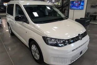Vue 3/4 avant droite d'un Volkswagen Caddy blanc 2025 en showroom avec calandre noire et phares LED.