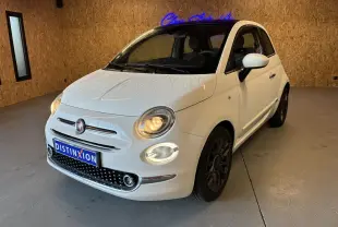 Vue 3/4 avant d'une Fiat 500 blanche de 2021 avec phares allumés et jantes foncées dans un garage.