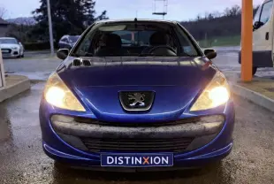 Vue avant d’une Peugeot 206+ bleue de 2011 avec phares allumés et plaque Distinxion visible.