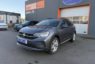 Volkswagen Taigo 2025 gris INC en 3/4 avant droit, avec jantes alliage et toit noir visible devant un bâtiment commercial.