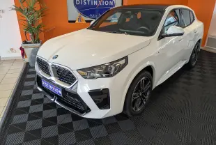 BMW X2 sDrive blanc alpin vue de profil côté gauche, avec jantes sport et toit panoramique en intérieur showroom.