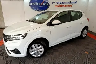 Vue 3/4 avant d'une Dacia Sandero Confort TCe 90 blanche, stationnée en intérieur sur sol damier noir et rouge.