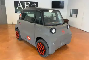 Vue 3/4 avant droite d'une Citroën AMI Spicy grise électrique 2025 avec jantes et logos orange distinctifs.