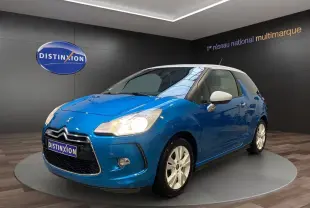 Citroën DS3 bleu avec toit blanc en 3/4 avant droit, phare allumé et jantes blanches visibles en showroom.