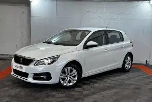 Peugeot 308 blanche vue 3/4 avant droit dans un garage avec phares allumés et jantes alliage.