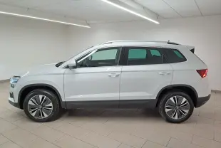 Vue de profil côté gauche du Skoda Karoq blanc Lune 2025 avec jantes spécifiques et rampes de pavillon argent visibles.