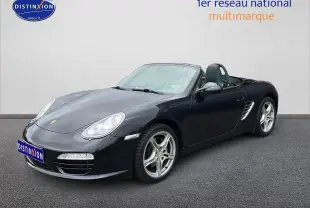 Vue 3/4 avant droite d'une Porsche Boxster 987 noire cabriolet avec jantes alu 17 pouces sur sol gris.