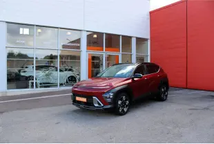 Hyundai Kona 2024 rouge Ultimate Metal avec toit noir, vu en 3/4 avant droit devant un bâtiment commercial.