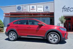 Vue de profil côté gauche d'un Volkswagen Taigo rouge roi garé devant un service auto multimarques.