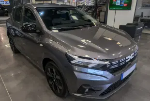 Vue 3/4 avant d'une Dacia Sandero TCe 90 gris schiste en showroom, avec jantes noires et calandre distinctive.