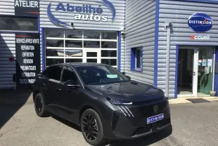 Peugeot 3008 gris titane en 3/4 avant droit devant un garage avec logo Abeilhé autos visible.