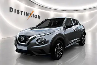Nissan Juke gris 3/4 avant droit en showroom avec jantes alu et calandre chromée distinctive.