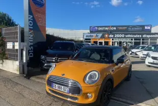 Vue 3/4 avant d'une MINI Cooper D orange 2015 avec toit noir, garée devant un concessionnaire automobile.