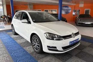 Volkswagen Golf blanc vue 3/4 avant droit dans un showroom avec jantes alliage et phares LED allumés.