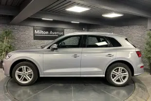 Profil côté gauche d'un Audi Q5 gris métallisé S line 2019 dans un showroom avec jantes 5 branches doubles.