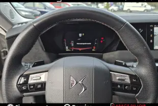 Vue rapprochée du volant cuir DS avec commandes tactiles, affichage numérique du tableau de bord en arrière-plan.