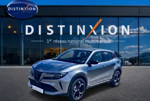 Vue 3/4 avant d'un Alfa Romeo Junior gris avec jantes alliage noires et toit noir devant une vitrine Distinxion.