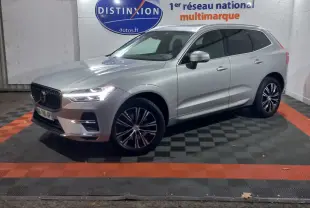 Volvo XC60 B4 gris clair vu de 3/4 avant droit, avec jantes alliage et phares LED allumés en intérieur showroom.