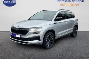 Vue 3/4 avant droite d’un Skoda Karoq argent 2025 avec barres de toit et jantes noires distinctives.