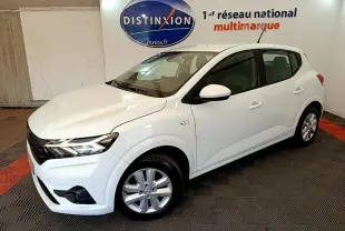 Vue 3/4 avant droit d'une Dacia Sandero Confort TCe 90 blanche, avec phares LED et jantes alliage en intérieur showroom.