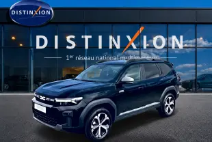 SUV Dacia Bigster noir en 3/4 avant droit avec jantes alliage diamantées et barres de toit visibles devant vitrine Distinxion.