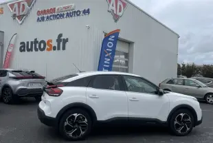 Vue de profil côté gauche d'une Citroën C4 X blanche avec jantes alliage noires devant un garage auto.