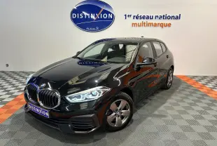 BMW Série 1 16d noire vue en 3/4 avant droit, phares LED allumés, sur sol damier gris et orange en showroom