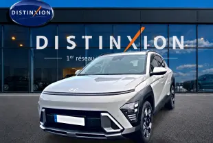Hyundai Kona hybride gris en 3/4 avant droit, avec jantes alliage et calandre épurée devant un showroom Distinxion.