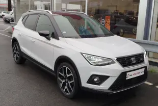 SEAT Arona blanc avec toit gris magnétique, vue 3/4 avant droit, feux allumés et jantes alliage noires.
