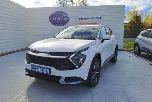 KIA SPORTAGE blanc vu en 3/4 avant droit, avec calandre noire distinctive et jantes bi-ton sur parking extérieur.