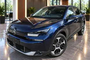 Citroën C4 1,2 Hybrid 2025 bleu eclipse vue 3/4 avant en intérieur avec jantes distinctives et éclairage LED.