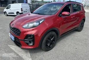 KIA SPORTAGE rouge métal vu en 3/4 avant droit, avec jantes noires et détails Black Edition visibles sur carrosserie.