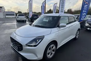 Suzuki Swift 1.2 Privilège blanc vue 3/4 avant droit avec calandre noire et feux LED allumés sur parking.