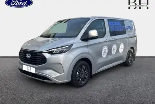 Ford Transit Custom gris lunaire métallisé vu en 3/4 avant droit avec marquages publicitaires sur la porte latérale.